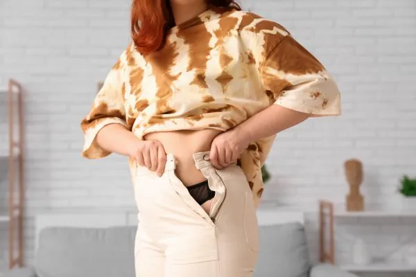 Image of woman trying to do her trousers up after pregnancy weight gain Witney