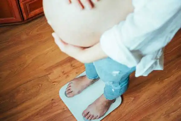 Image of woman weighing herself and experiencing weight gain through pregnancy Witney