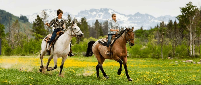 Confident plus-size woman riding Witney a horse through a field with a smile on her face.